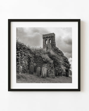 Black and white photograph of ivy-covered church ruins and headstones in Cahir, Ireland.