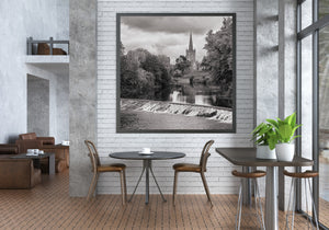 Cahir riverside scene combining a tall church spire, dense trees and moving water.