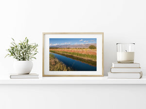 Colour landscape photograph of a blue river, grassy banks and distant mountain ridges.