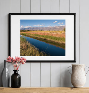 California countryside with a narrow waterway and golden vegetation beneath a blue sky.