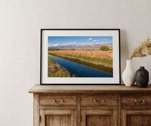 Distant mountains stretch beyond a blue river running through sunlit grasses.