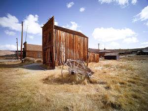 An abandoned Old West building rises from dry grasses in a sunlit California ghost town.