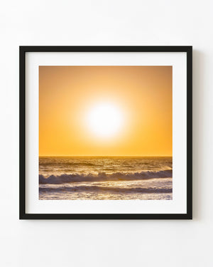 A golden sun glows above breaking surf along the California coast.