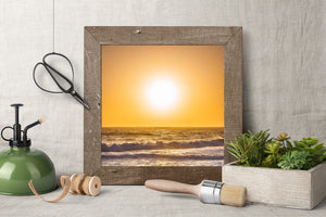 A brilliant sun hangs above a dark ocean horizon and bands of foaming surf.