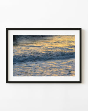 Golden reflections spread across blue-grey Pacific surf along the California coast.