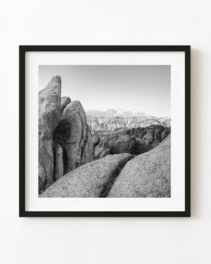 Black and white California landscape with rugged rock formations and distant snowy mountains.