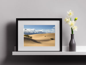 A broad dune landscape contrasts golden sand with blue sky and scattered clouds.