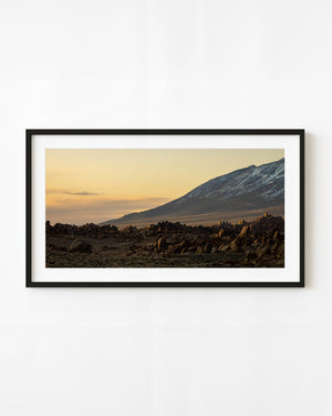 Warm sunset light falls above rocky California terrain and a snow-streaked mountain slope.