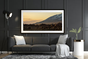 Snow traces a distant mountain slope beyond scattered rocks beneath fading golden light.
