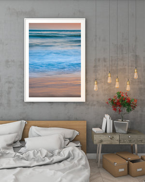 Foaming Pacific waves soften into blue layers beneath a peach evening sky.