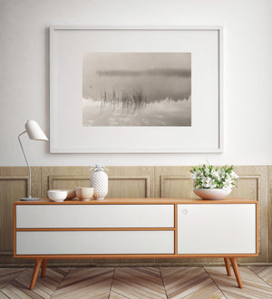 Minimalist nature photograph of pale mist, quiet water and fine grass stems.