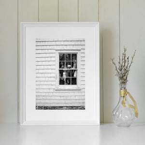 Pale wooden shingles contrast with dark window panes filled with maritime objects.