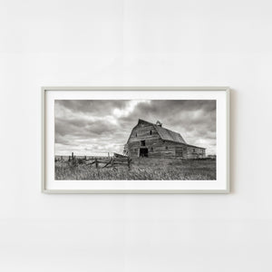 Abandoned wooden barn in Saskatchewan under dramatic storm clouds in monochrome