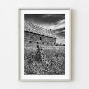 Black and white prairie barn with leaning fence in tall grass Saskatchewan