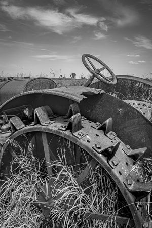 Black and white photo of abandoned farm tractor parts in field