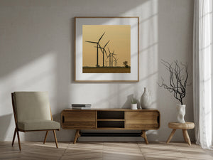Wind turbines stand above a dark field against an amber evening sky.