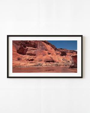Red sandstone cliffs at Canyon de Chelly in Arizona beneath a clear blue sky.