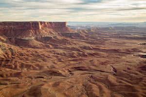 Broad sandstone cliffs stand above intricately eroded ridges in a wide Utah landscape.