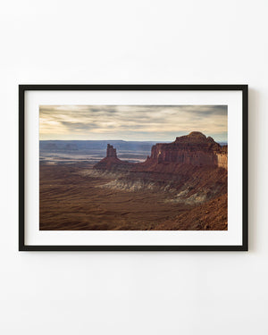 Red rock buttes rise above a rugged Canyonlands landscape beneath golden clouds.