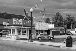 A vintage Volkswagen Beetle sits outside Carol’s Corner diner beneath roadside signs.