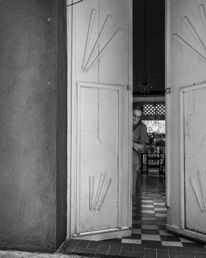 Tall pale doors open onto a shaded Cartagena interior with a woman visible inside.