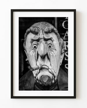 Black and white photograph of an expressive carved wooden face holding a cigar.