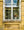 White window frames and lace curtains surround flowers and a cat behind the glass.