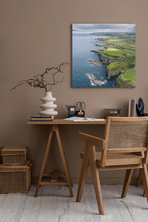 Square aerial landscape photograph with green fields above rocky sea cliffs.