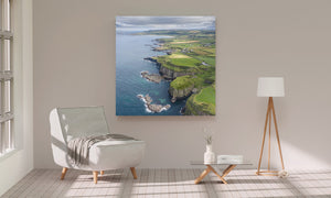 Patchwork fields stretch inland from a winding coastline beside blue grey sea.
