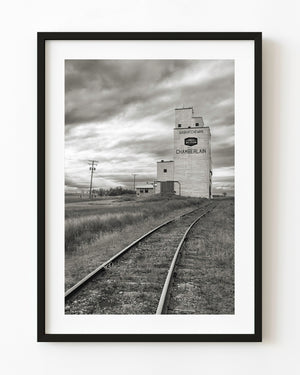 Black and white photograph of railway tracks leading toward a grain elevator in Chamberlain, Saskatchewan.