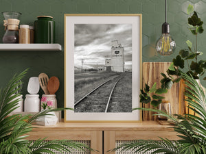 Vertical Saskatchewan landscape with a weathered grain elevator and converging railway lines.
