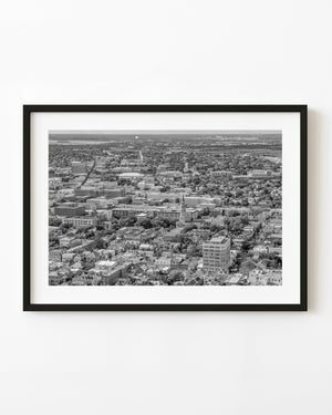 Black and white aerial photograph of Charleston rooftops, streets and trees extending toward the horizon.