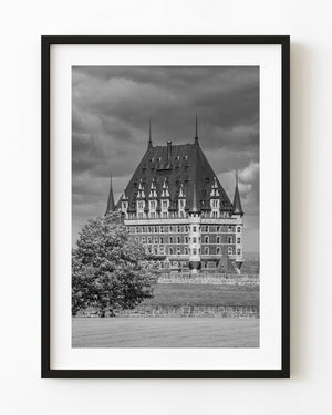 Chateau Frontenac rooflines rise beneath dramatic clouds in a black and white Quebec City photograph.