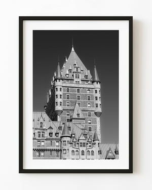 Chateau Frontenac tower and pointed turrets rise against a dark sky in black and white.