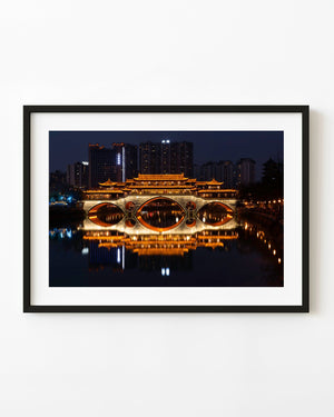 An illuminated bridge and golden river reflections glow beneath a dark Chengdu evening skyline.