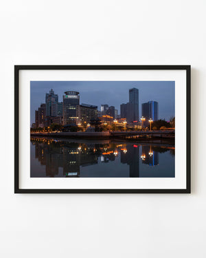 Chengdu riverside skyline reflects in calm water beneath a blue hour sky with warm city lights.