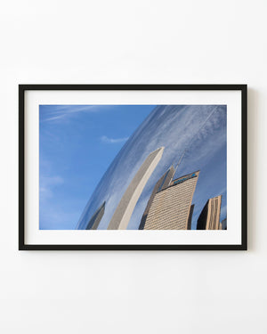 Chicago buildings reflect across the curved surface of the Bean sculpture beneath a blue sky.