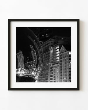 Black and white night photograph of Chicago buildings curving across reflections in the Bean sculpture.
