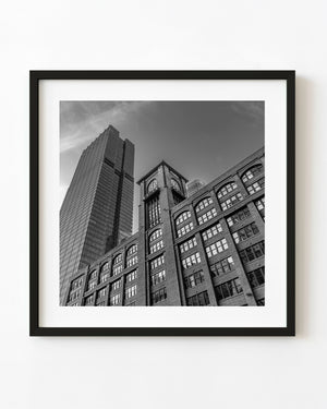 Black and white Chicago clock-tower architecture rises beside a modern skyscraper from a low viewpoint.