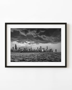 Black and white photograph of Chicago’s skyline beneath sweeping storm clouds across Lake Michigan.