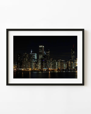 Chicago skyline at night with illuminated towers and golden waterfront lights reflected on Lake Michigan.