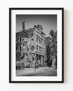 Black and white Chicago street photograph of a mural-covered brick building beside a sidewalk.
