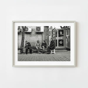 Elderly women and man sitting outside a restaurant on a Beijing street in black and white