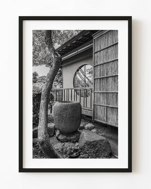 Black and white Chofu Garden photograph with a circular window, wooden wall, tree and stone basin.