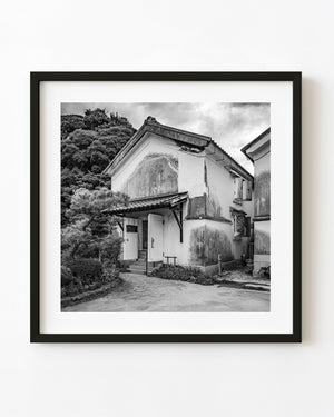 Black and white photograph of a weathered Japanese kura storehouse in Chofu with a tiled roof and garden path.