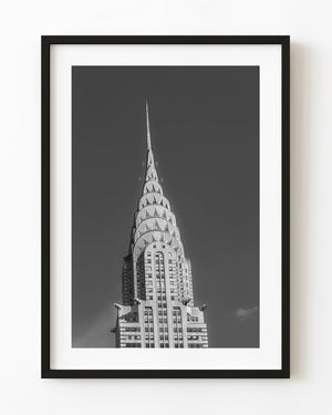 Black and white photograph of New York’s Chrysler Building crown and spire against an open sky.