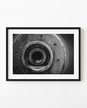 Black and white close-up of heavy machinery with concentric metal rings and a dark circular opening.