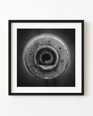 Black and white industrial photograph of a circular machine opening surrounded by textured metal and small holes.