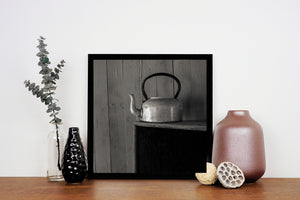 A curved kettle handle and short spout stand out against muted wooden boards in black and white.