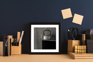 Monochrome teapot photograph with bright metal surfaces above a deep rectangular cabinet shadow.